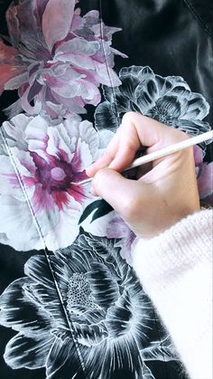 a woman is drawing flowers on a black and white floral print dress with a pencil