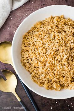 a white bowl filled with brown rice next to two spoons