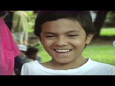 a young boy smiling at the camera with other children in the back ground behind him