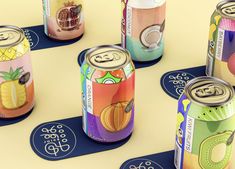 several cans of various types of drinks on top of blue coasters with fruit and pineapple designs