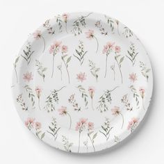 a white plate with pink flowers and green leaves on the rim, against a white background