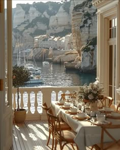 an outdoor dining area with tables and chairs overlooking the water's edge, along with boats in the bay