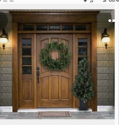 two christmas wreaths sit on the front door of a house, with lights on either side