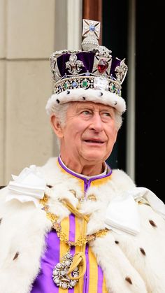 an older man wearing a regal crown and fur coat, standing in front of a building