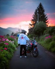 a person standing next to a motorcycle on a dirt road at sunset with mountains in the background