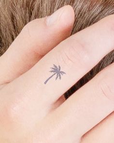 a person with a small palm tree tattoo on their left hand and the other finger