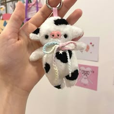 a hand holding a small stuffed cow keychain in it's right hand