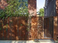 a wooden gate in front of a brick building with trees growing on the side walk