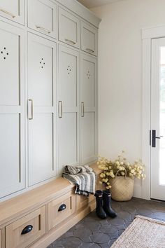 an entryway with lots of white cabinets and flowers in a vase on the bench