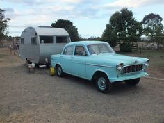 an old blue car is parked in front of a trailer with a camper behind it