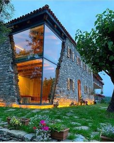 a house made out of stone and glass in the middle of a grassy area with trees