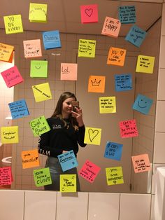 a woman standing in front of a mirror covered in sticky notes