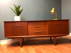 a wooden sideboard with two drawers and a lamp on the top, in front of a blue wall