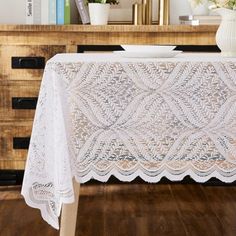 a white table cloth on top of a wooden dresser next to a vase with flowers