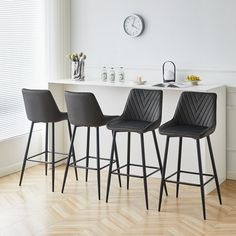 three black bar stools sitting in front of a white counter with a clock on the wall