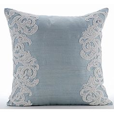 a light blue pillow with white lace on the front and back side, sitting on a white surface