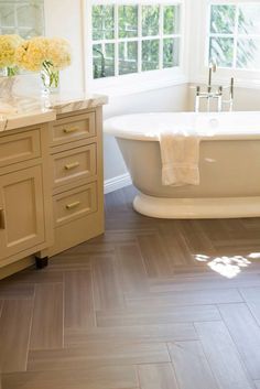 a white bath tub sitting next to a window in a bathroom with wooden floors and walls