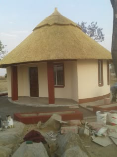 a small building with a thatched roof and red trim around the door, surrounded by large rocks