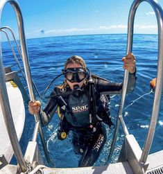 a woman scubas in the ocean while holding her hand up and looking at the camera