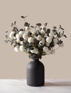 a black vase filled with white flowers on top of a marble countertop next to a gray wall