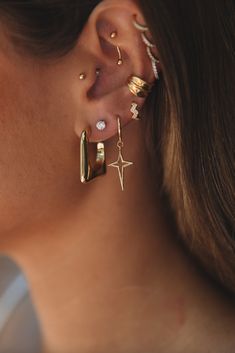 a close up of a person wearing gold ear cuffs and piercings on their ears