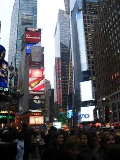 many people are walking on the street in new york city at night with tall buildings