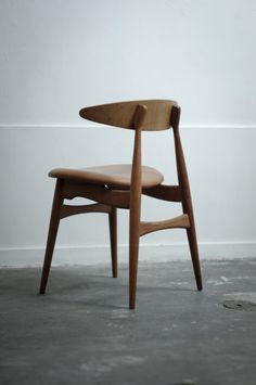 a wooden chair sitting on top of a cement floor in front of a white wall