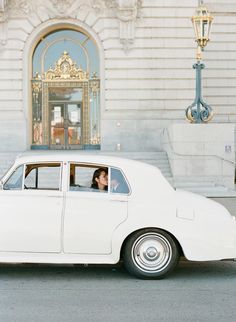 the bride and groom are sitting in an old white car on their wedding day, looking out the window