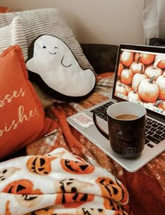 a laptop computer sitting on top of a bed next to a cup of coffee and a pillow