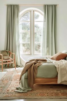 a bed sitting under a window next to a chair and table in front of a large window