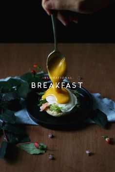 a person pouring mustard onto a sandwich on a black plate with leaves and flowers around it