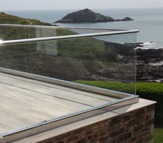 a balcony overlooking the ocean with a glass railing on it and an island in the distance