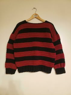 a red and black striped sweater hanging on a hanger with a white wall in the background