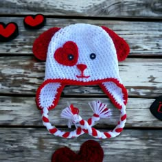 a crocheted hat with a red and white teddy bear on it, next to hearts