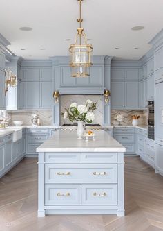 a large kitchen with blue cabinets and white counter tops, gold chandelier hanging from the ceiling