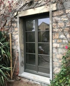 an old stone building with two windows and plants growing on the outside side of it