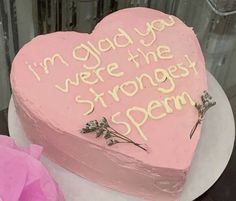 a pink heart shaped cake with writing on the side and flowers in front of it