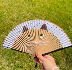 a hand holding an orange and white cat shaped fan on top of some green grass