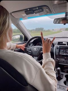 a woman driving a car with her hand on the steering wheel and pointing at something