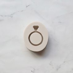 a white ring with a diamond on it sits on a marble surface in front of a marble background