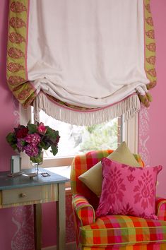 a colorful chair and table in front of a window with pink walls, curtains and flowers