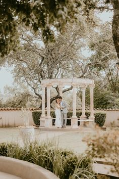 a bride and groom standing in front of a gazebo