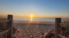 the sun is setting over the beach and ocean with wooden gates leading into the sand