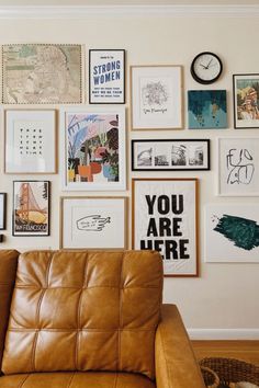 a brown leather couch sitting in front of a wall covered with pictures and framed art