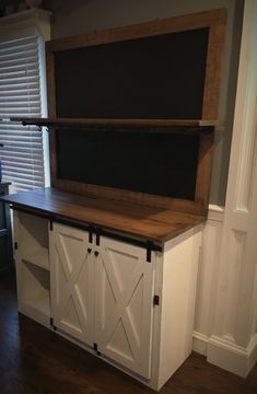 a kitchen island with sliding doors and a chalkboard on the top, in front of a window