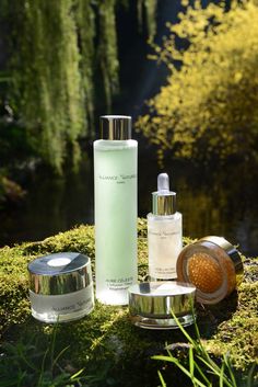 three different types of skin care products sitting on top of a mossy surface next to water