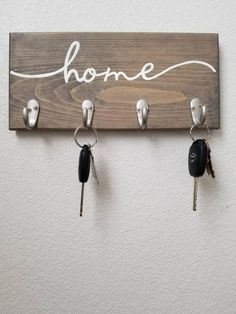 three keys hang on a wooden sign with the word home written in white lettering and four key hooks attached to it