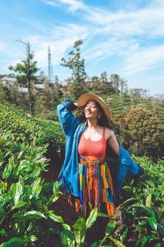 a woman standing in a field with her arms behind her head and wearing a hat