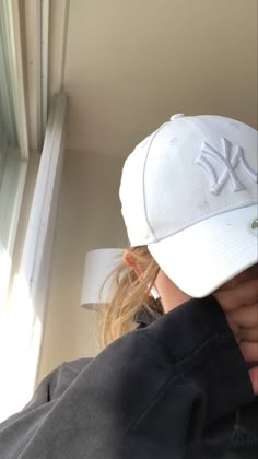 a woman wearing a new york yankees hat looking out the window with her hand on her shoulder