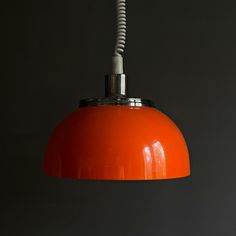 an orange pendant light hanging from a ceiling in a dark room with a black wall behind it